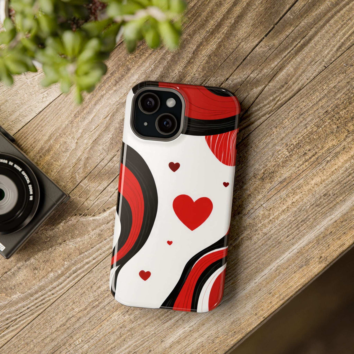 Phone case on wood surface: glossy red heart and swirl pattern in white with red and black waves.