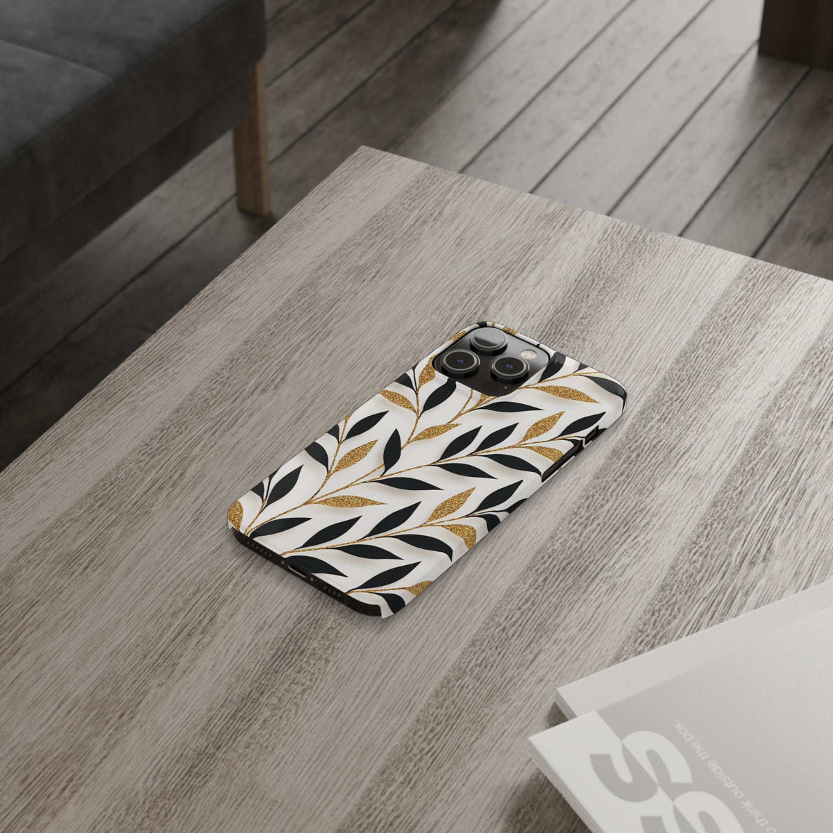 Botanical leaf phone case with gold accents, shown at an angle on a table