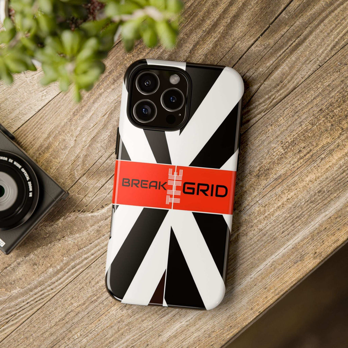 Break Grid phone case standing on wood, black-and-white stripes and orange “Break Grid” band