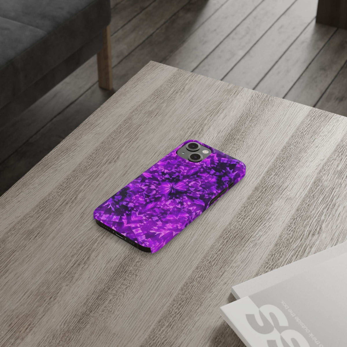 Purple kaleidoscope phone case lying on light wood, camera cutouts visible