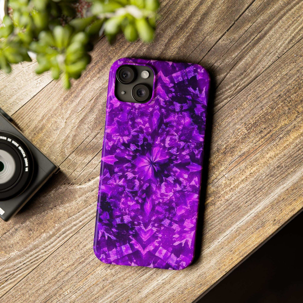 Purple kaleidoscope phone case with triple camera cutouts on a wood tabletop.