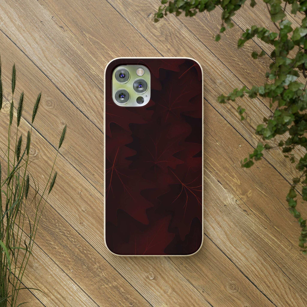 Burgundy autumn leaf phone case with camera cutouts, shown on wood tabletop