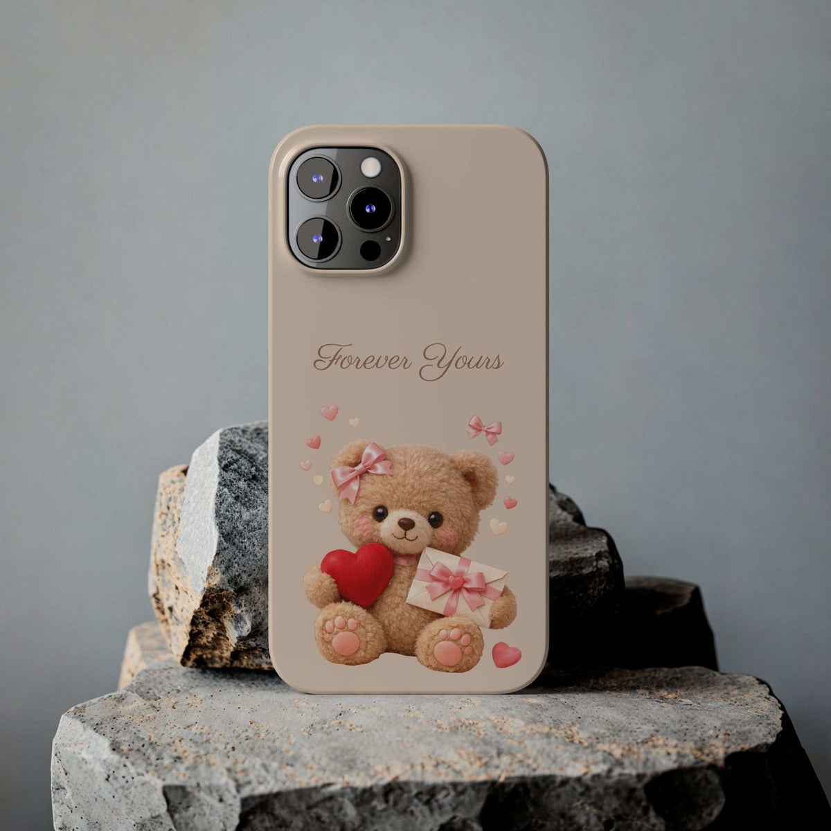 Beige phone case on stone pedestal with teddy bear holding red heart and pink gift, “Forever Yours”