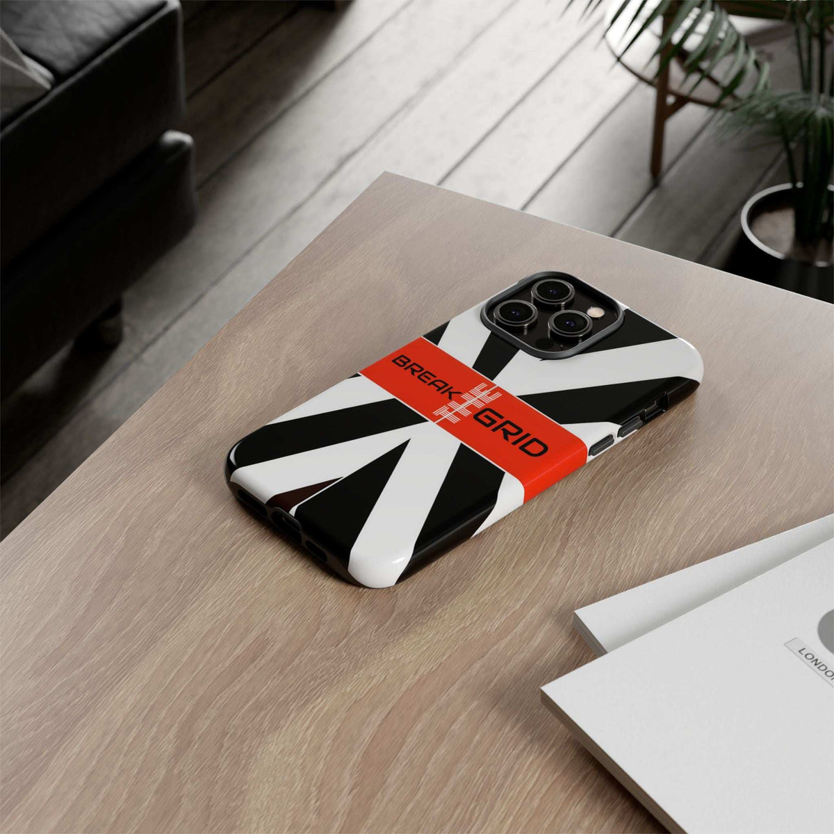 Break Grid phone case on a desk, black-and-white geometric design with orange “Break Grid” band