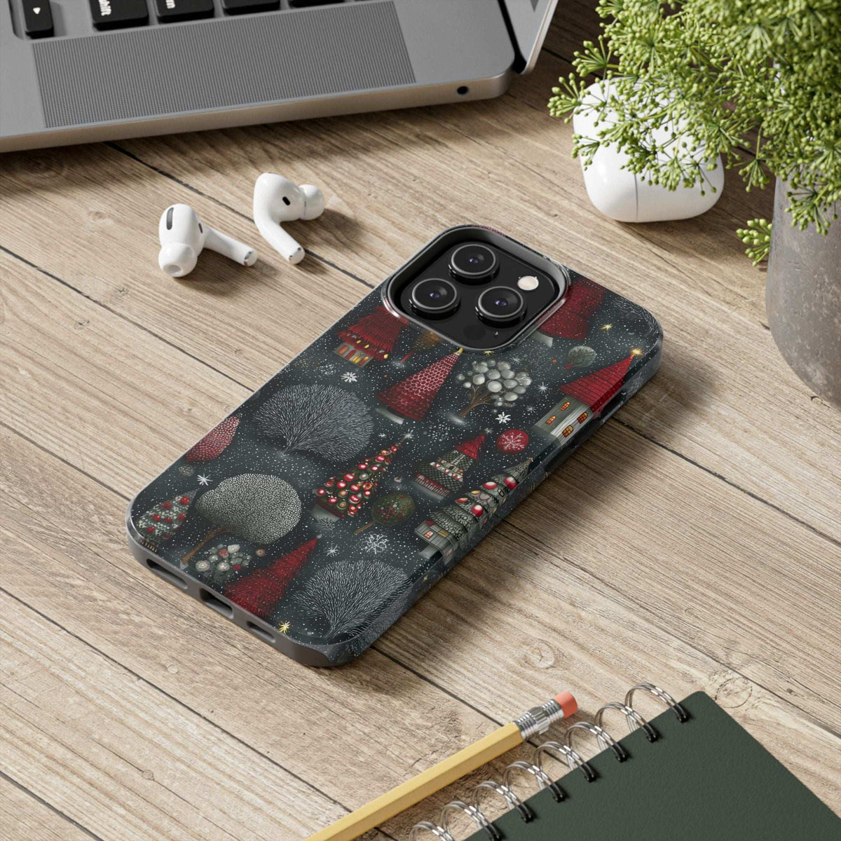Phone case on a wood desk with winter fir artwork and a visible raised camera area