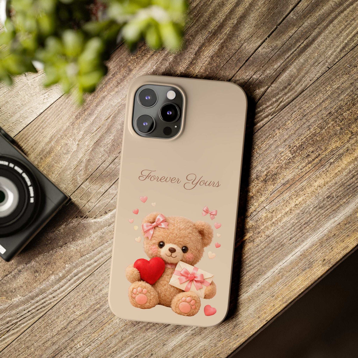 Beige phone case lying on wood, featuring teddy bear with red heart, gift box, “Forever Yours”